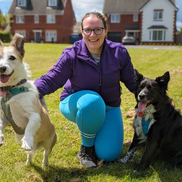 A woman with two dogs on a sunny day with houses in the background